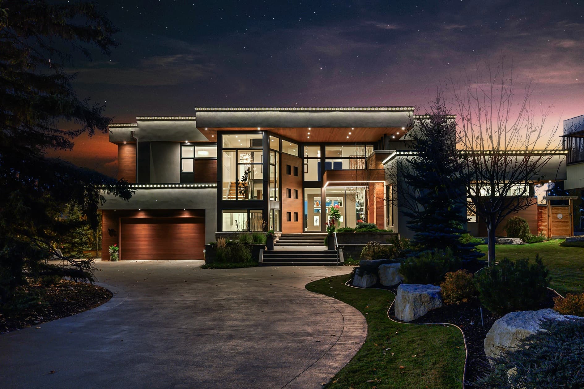 Modern estate home in Bel-Aire at night with warm interior lighting and a curved driveway