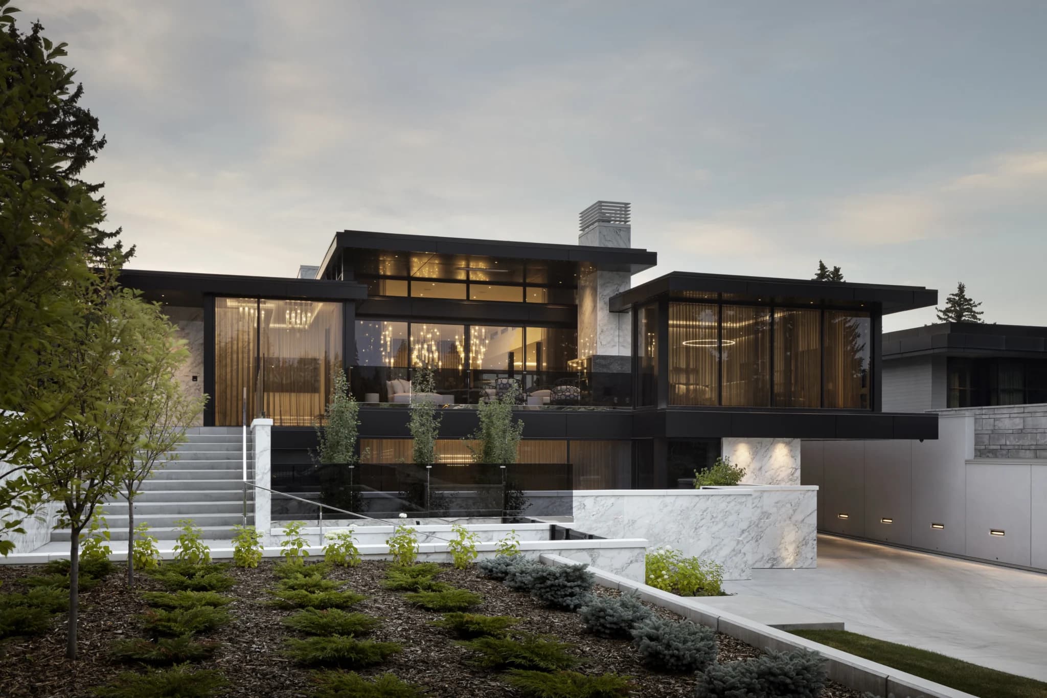 Contemporary glass-walled home in Britannia at dusk with landscaped terraces