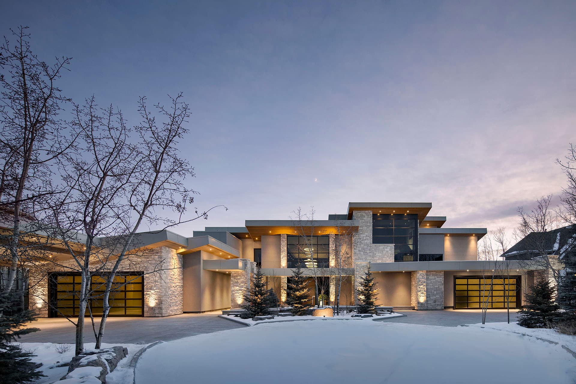 Modern stone-and-glass estate home in Upper Mount Royal at dusk, lit from within